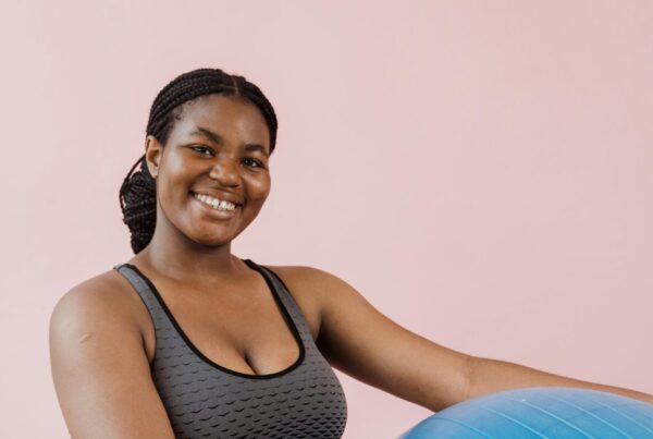 A young woman in athletic wear smiles while holding an exercise ball.