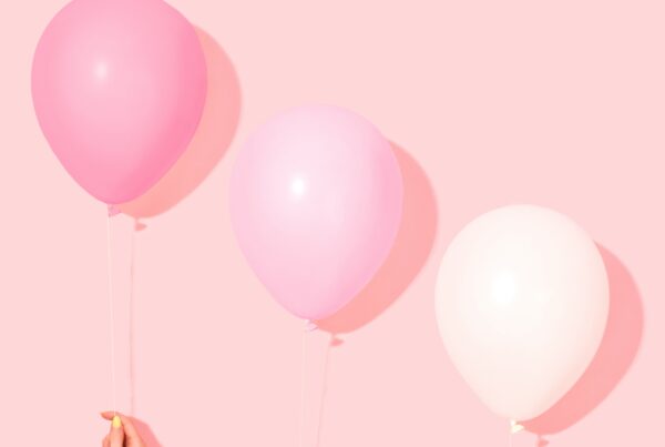 Three hands holding up three balloons.